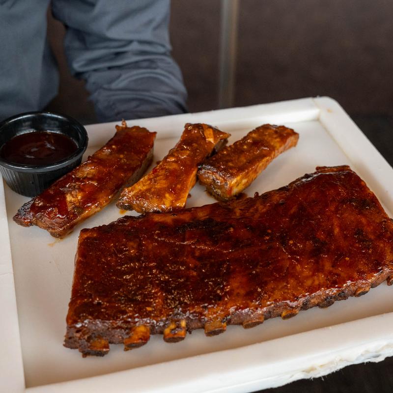 Barbecue pork ribs served with a side of dipping sauce on a white plate.
