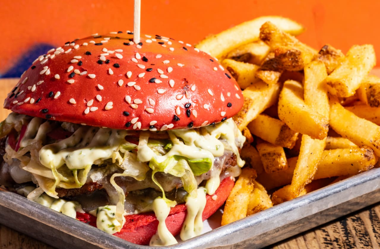 Image of a burger with a pink seeded bun, served with chips in collaboration with Breast Cancer Awareness Month
