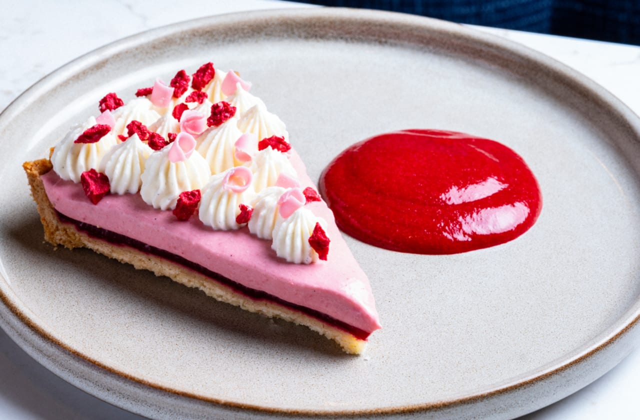 Raspberry and rose tart with whipped cream, freeze-dried raspberries and raspberry sauce on a ceramic plate.