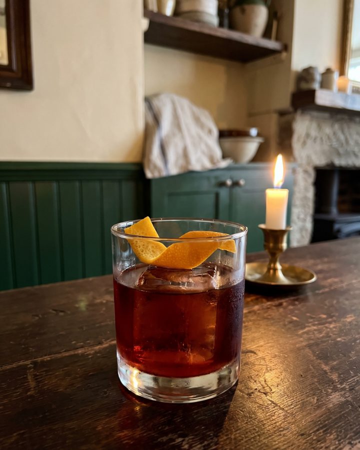 A dark stirred drink over one large cube in candlelight