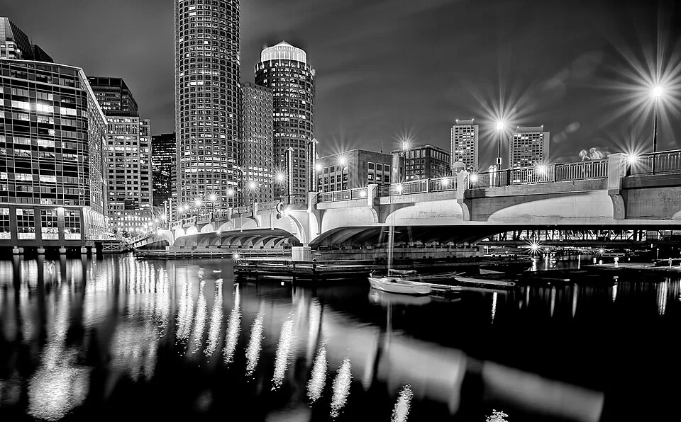 The lit Evelyn Moakley Bridge into the Seaport at night, reflected in Fort Point Channel